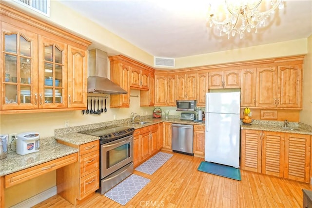 kitchen featuring light stone countertops, appliances with stainless steel finishes, wall chimney exhaust hood, and a chandelier