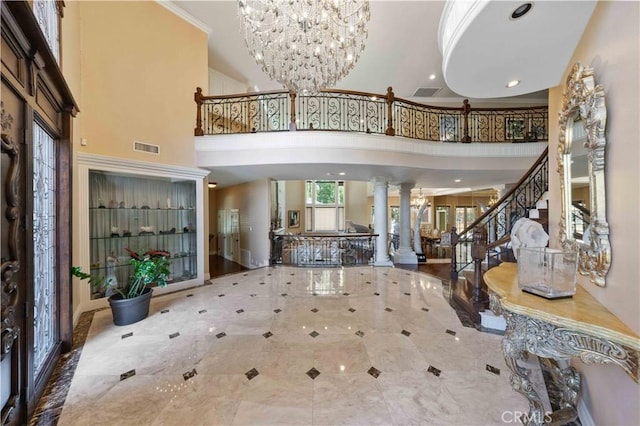 foyer entrance with ornate columns, crown molding, a towering ceiling, and a chandelier