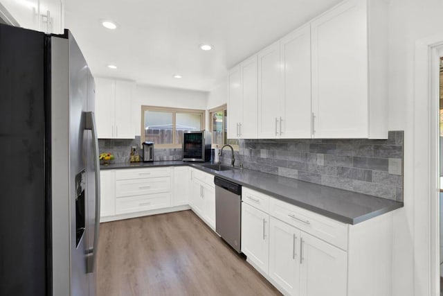 kitchen with sink, stainless steel appliances, white cabinets, decorative backsplash, and light wood-type flooring