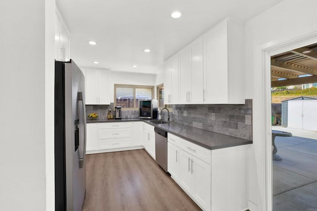 kitchen featuring sink, light hardwood / wood-style flooring, white cabinetry, stainless steel appliances, and tasteful backsplash