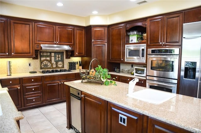 kitchen with decorative backsplash, light tile patterned floors, built in appliances, and light stone counters