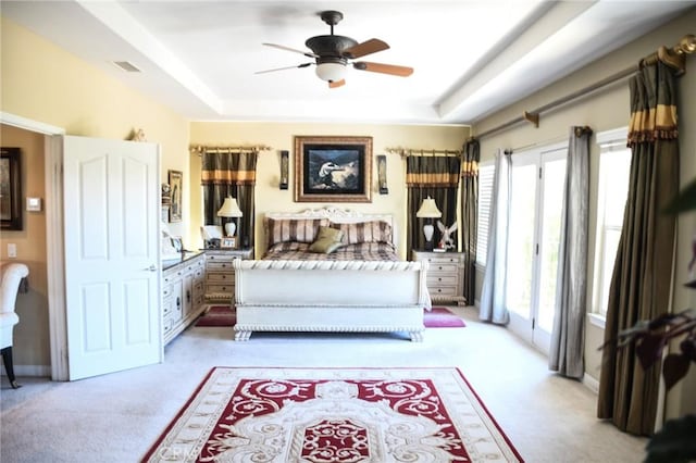 living area featuring light carpet, a raised ceiling, ceiling fan, and a healthy amount of sunlight