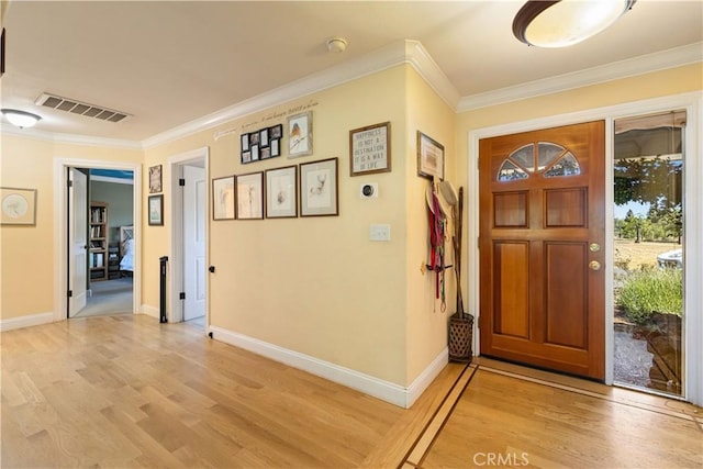 foyer entrance featuring visible vents, crown molding, light wood-style flooring, and baseboards