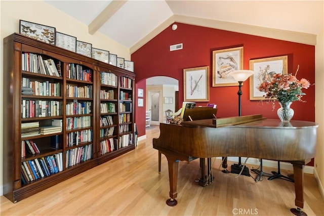 sitting room featuring baseboards, visible vents, arched walkways, wood finished floors, and vaulted ceiling with beams