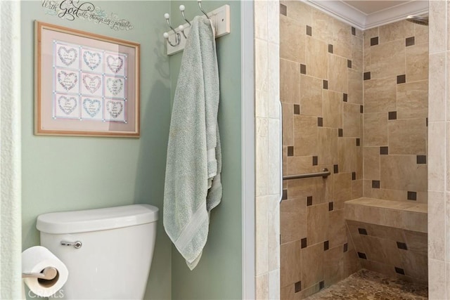 bathroom with toilet, ornamental molding, and a tile shower