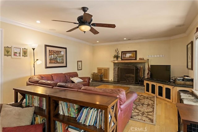 living room with light wood finished floors, ceiling fan, ornamental molding, and a fireplace with raised hearth