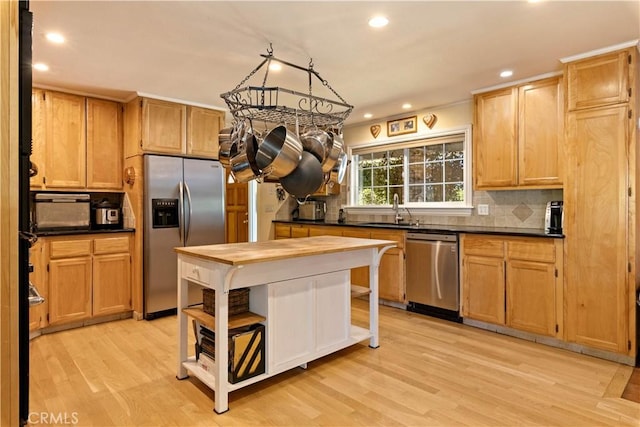 kitchen featuring dark countertops, appliances with stainless steel finishes, a sink, light wood-style floors, and backsplash