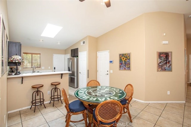 dining space with ceiling fan, lofted ceiling with skylight, sink, and light tile patterned floors