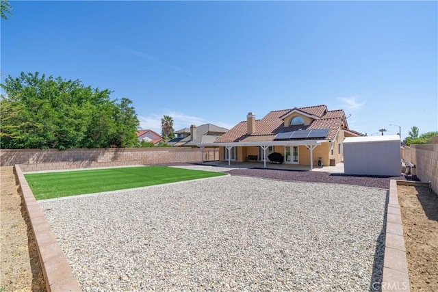 rear view of house with a lawn, solar panels, and a patio