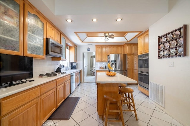 kitchen featuring a breakfast bar area, tasteful backsplash, a tray ceiling, a kitchen island, and appliances with stainless steel finishes