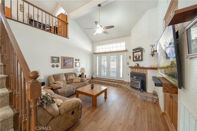 living room featuring a wood stove, high vaulted ceiling, french doors, ceiling fan, and light wood-type flooring