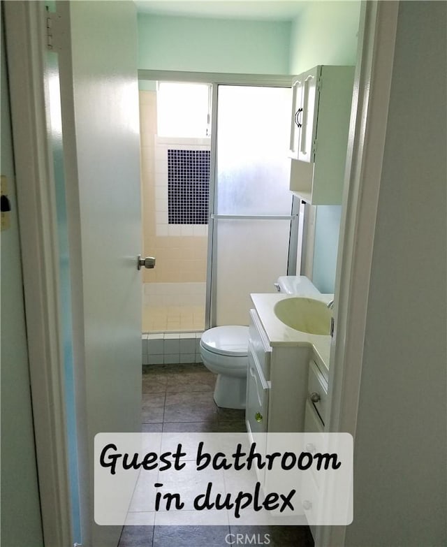 bathroom with tile patterned flooring, vanity, toilet, and walk in shower