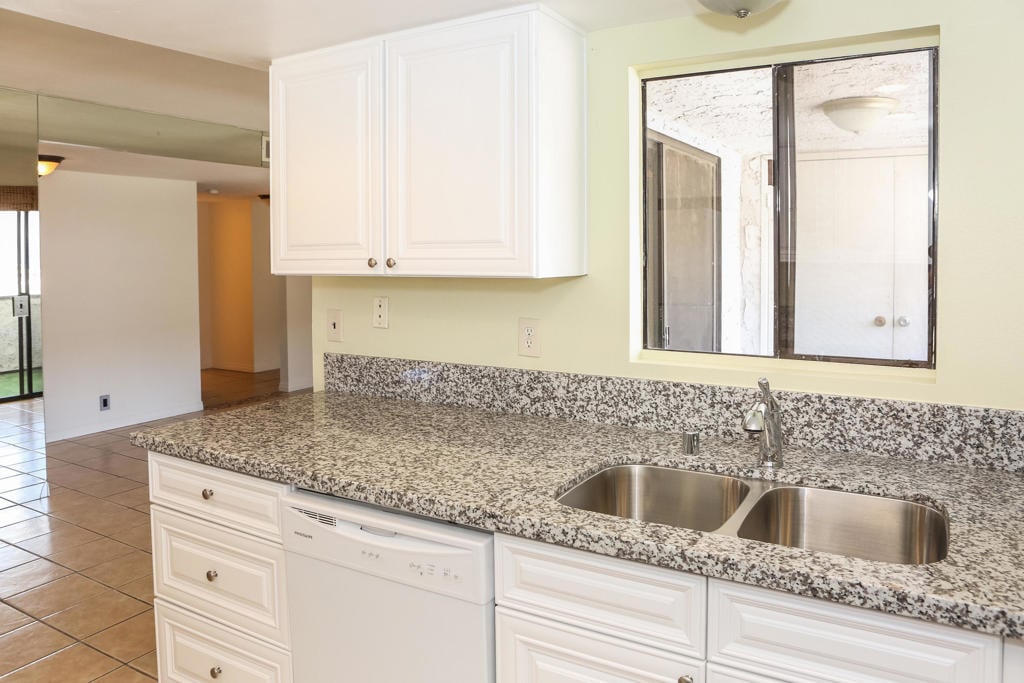 kitchen featuring light tile patterned floors, white cabinetry, white dishwasher, and light stone counters