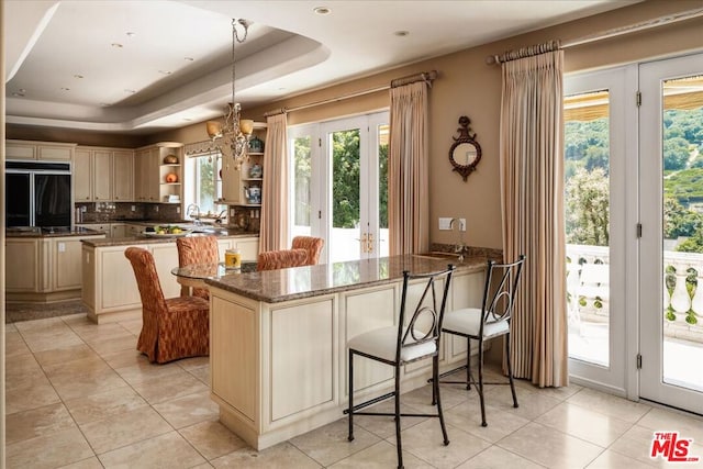 kitchen with a kitchen island, light tile patterned floors, built in fridge, a tray ceiling, and dark stone counters