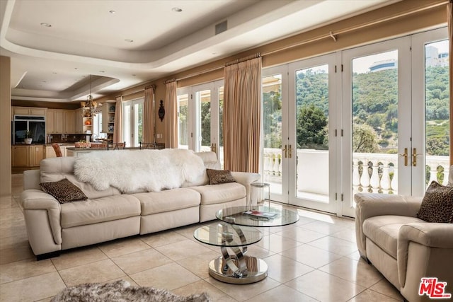 tiled living room featuring a notable chandelier, a raised ceiling, and plenty of natural light