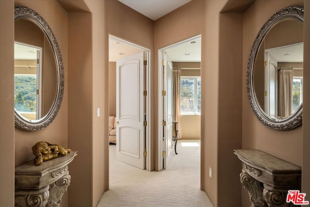 hall featuring light colored carpet and plenty of natural light