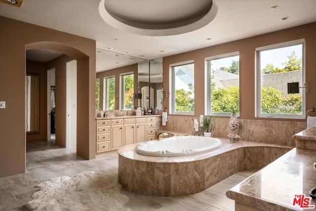 bathroom featuring a tray ceiling, tiled bath, and vanity