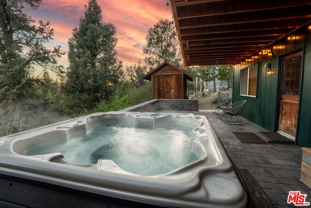 pool at dusk with a shed, a hot tub, and a patio area