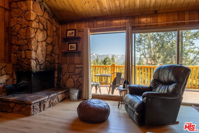 sitting room with a mountain view, wooden ceiling, wooden walls, hardwood / wood-style flooring, and a fireplace