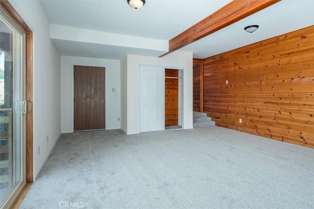 carpeted empty room with stairs, wood walls, and beam ceiling