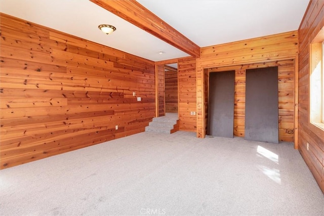 carpeted spare room with beam ceiling and wooden walls