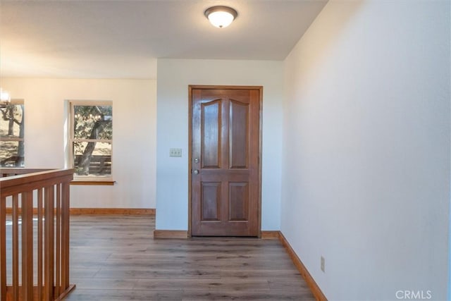 hallway featuring an inviting chandelier, wood finished floors, and baseboards