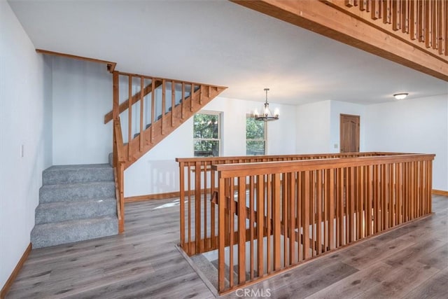 stairway with an inviting chandelier, baseboards, and wood finished floors