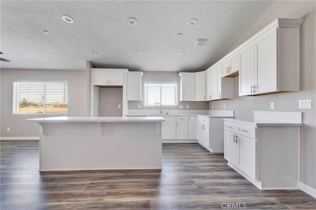 kitchen featuring white cabinets, dark wood-type flooring, a kitchen island, and a healthy amount of sunlight