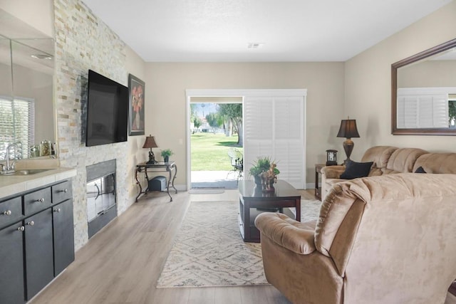 living room with light hardwood / wood-style floors, a stone fireplace, a wealth of natural light, and sink