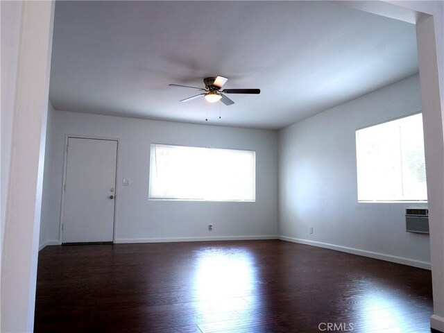 spare room with an AC wall unit, dark hardwood / wood-style flooring, ceiling fan, and a healthy amount of sunlight