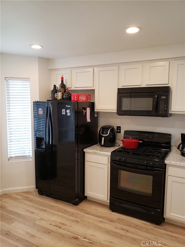 kitchen with light stone counters, white cabinetry, light hardwood / wood-style flooring, and black appliances