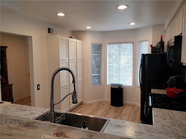 kitchen with gas stove, light stone countertops, sink, light hardwood / wood-style floors, and white cabinets