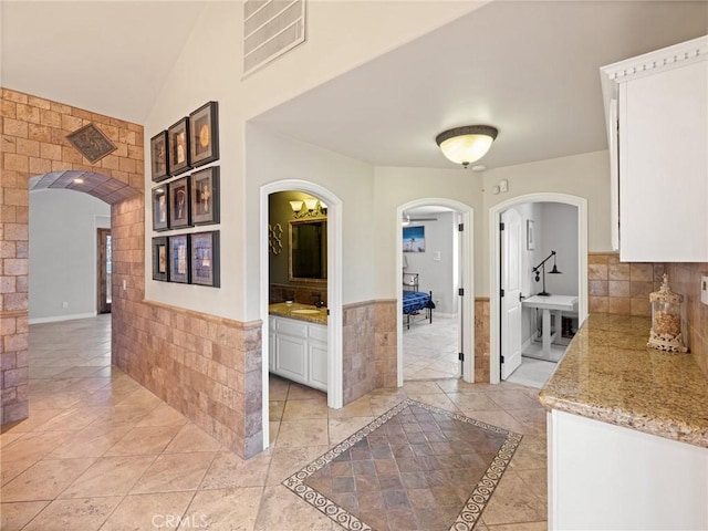 hallway with a sink, visible vents, arched walkways, and lofted ceiling