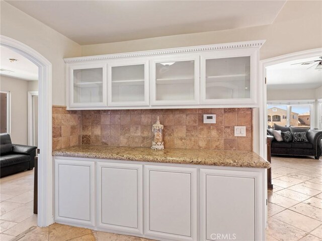 bar featuring ceiling fan, light stone countertops, decorative backsplash, and white cabinetry