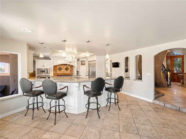 kitchen with built in appliances, light stone countertops, backsplash, a breakfast bar, and white cabinets