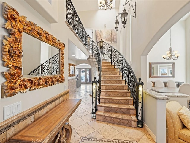 staircase featuring tile patterned flooring, baseboards, an inviting chandelier, a towering ceiling, and arched walkways