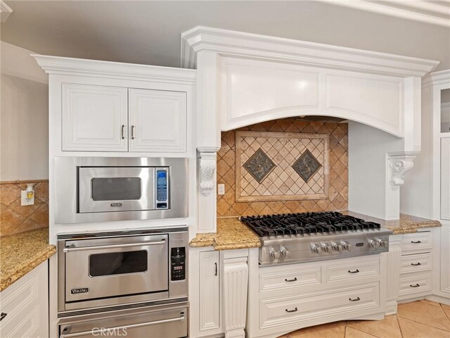 kitchen featuring stainless steel appliances, light stone countertops, backsplash, and white cabinetry