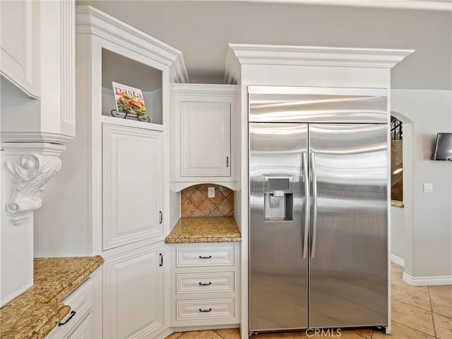 kitchen with light stone countertops, light tile patterned flooring, stainless steel built in fridge, white cabinets, and tasteful backsplash