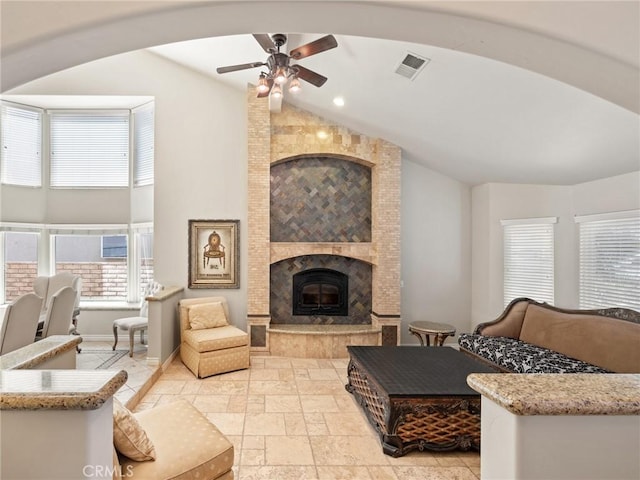 living area with a tiled fireplace, visible vents, arched walkways, and stone tile flooring