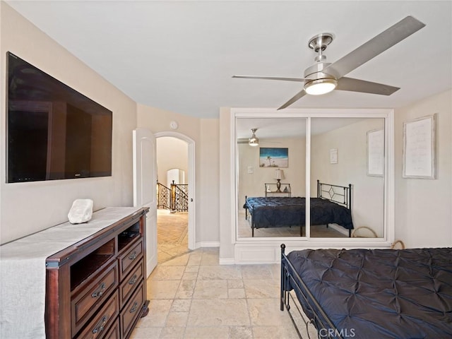 bedroom with ceiling fan, baseboards, arched walkways, and stone tile flooring