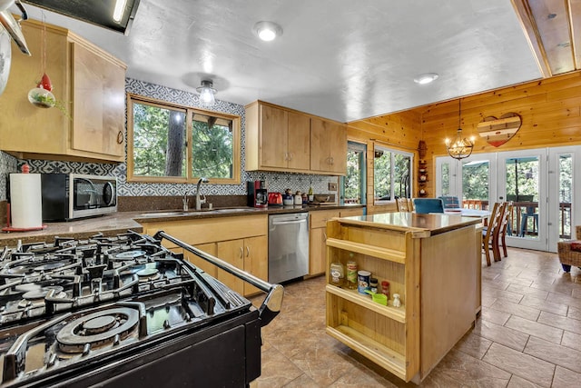 kitchen featuring appliances with stainless steel finishes, hanging light fixtures, light tile patterned flooring, wood walls, and sink