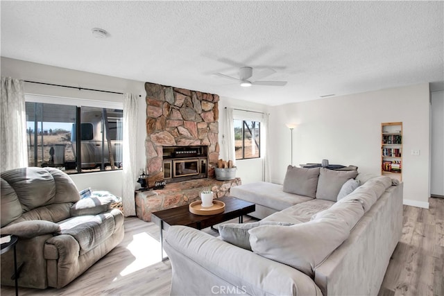 living room with light hardwood / wood-style floors, ceiling fan, a textured ceiling, and a fireplace