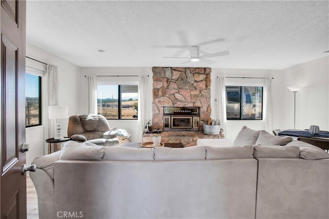 living room featuring ceiling fan, wood-type flooring, a textured ceiling, and a stone fireplace