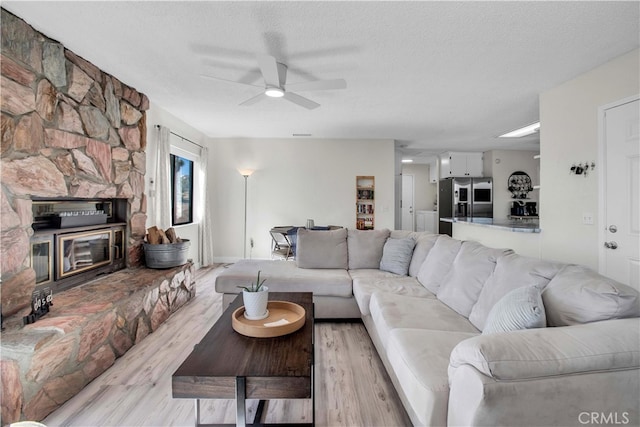 living room featuring a fireplace, ceiling fan, light hardwood / wood-style floors, and a textured ceiling