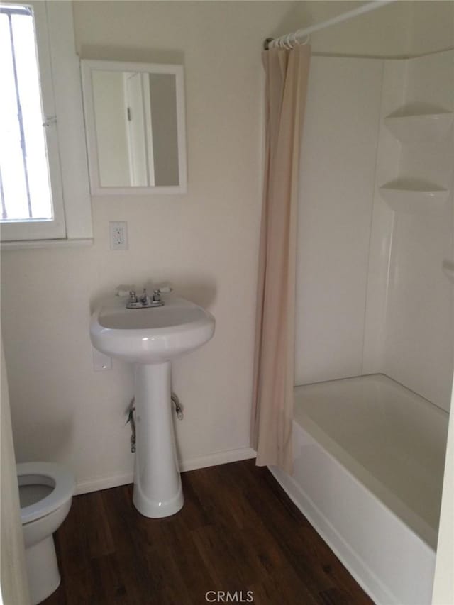 bathroom with hardwood / wood-style floors, toilet, and shower / bathtub combination with curtain