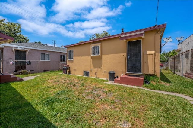 rear view of house with fence, a lawn, and stucco siding