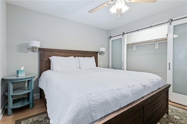 bedroom featuring a closet, a barn door, dark hardwood / wood-style floors, and ceiling fan