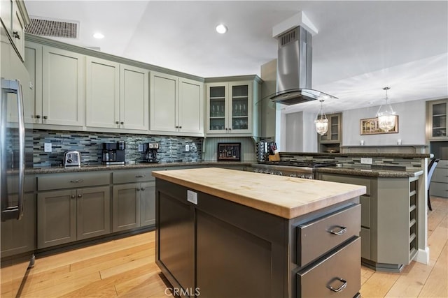 kitchen with kitchen peninsula, island range hood, decorative light fixtures, a center island, and butcher block countertops