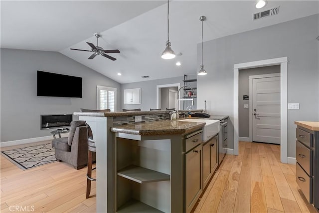 kitchen with decorative light fixtures, dark stone countertops, lofted ceiling, and a kitchen island with sink