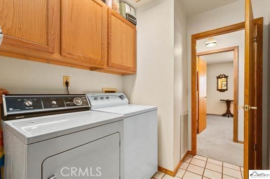 clothes washing area featuring cabinets, independent washer and dryer, and light tile patterned flooring